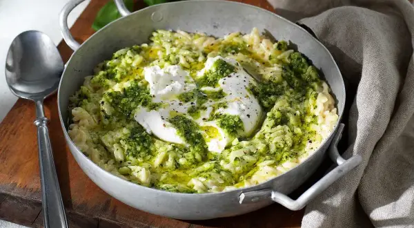 En skål med pasta som ser ut som ris, toppad med krämig burrata och grön pesto. En utsökt rätt som ser ut att vara gjord med kärlek.