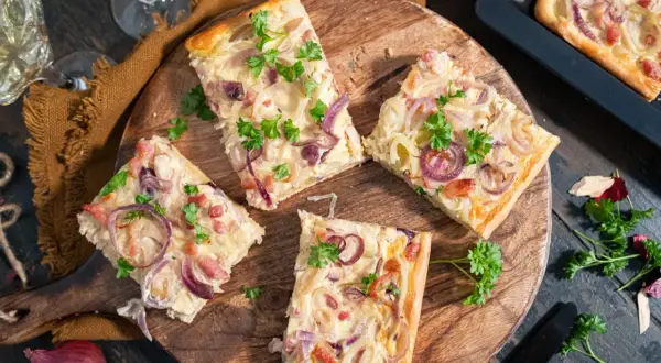 Saftiger Zwiebelkuchen vom Blech, belegt mit roten Zwiebeln und Speck, garniert mit Petersilie.