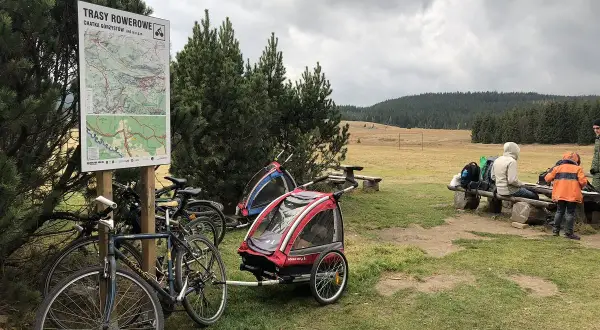 Góry Izerskie rowerem: mapa tras, rowery z przyczepkami i ludzie odpoczywający na ławce.