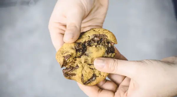 Hände halten einen weichen Chocolate Chip Cookie, der gerade zerbrochen wurde. Das Innere ist voller geschmolzener Schokolade. Ein perfektes soft cookies rezept!