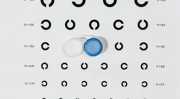 Tabela optometryczna z cyframi i otwartymi okręgami, obok pojemnik na soczewki kontaktowe.