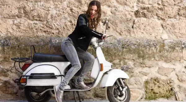Joven con chaqueta de cuero y jeans sobre una scooter blanca, lista para el mantenimiento de su scooter 125.