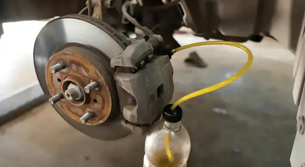 Proceso de purgar frenos: un tubo amarillo conecta la pinza de freno a una botella para extraer el líquido.
