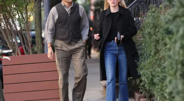 Coppia passeggia, lui con gilet e fascia, lei con cappotto e jeans a zampa. Un look che ricorda lo stile di Calvin Klein stilista.