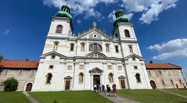 Majestatyczny klasztor Ojców Kamedułów na Bielanach z zielonymi kopułami wież, pod błękitnym niebem z chmurami.