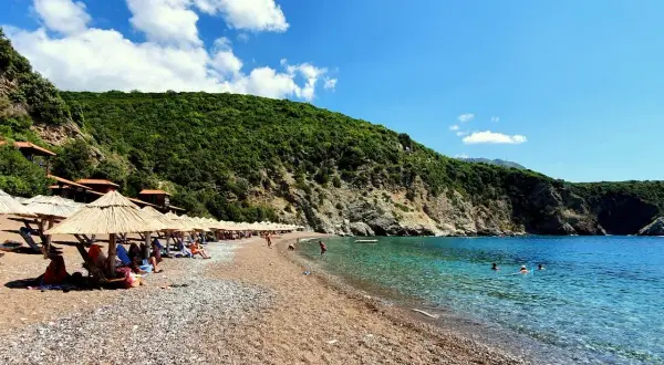 Słoneczne plaże w Budvie, z kamyczkami i piaskiem, otoczone zielonymi wzgórzami. Krystalicznie czysta woda Adriatyku zaprasza do kąpieli.
