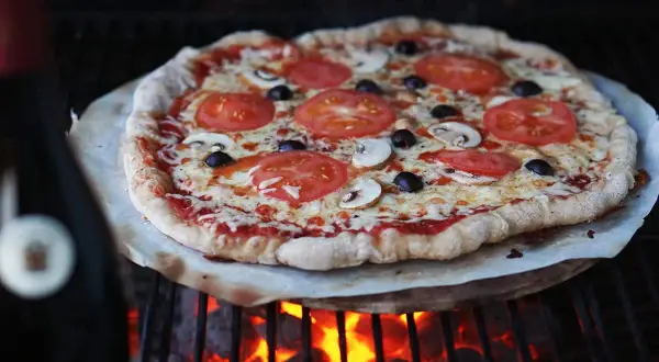 En härlig pizza på grillen med tomater, champinjoner och oliver. Glödande kol under ger en perfekt krispig botten.