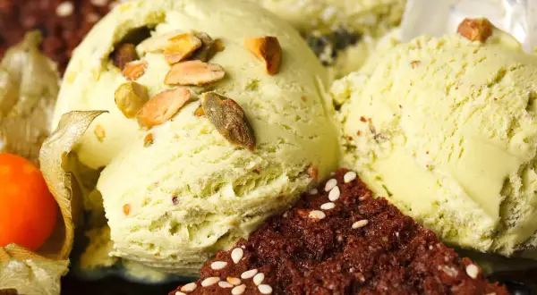 Cremiges veganes Eis selber machen: Pistazieneis mit Nüssen und Schokostückchen, garniert mit Physalis.