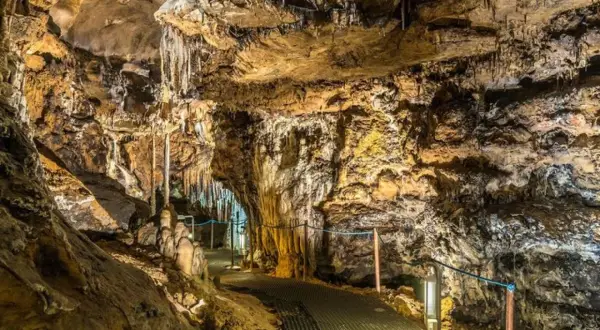 Interior de cuevas cerca de Madrid, con estalactitas y estalagmitas iluminadas, y un sendero metálico para visitantes.