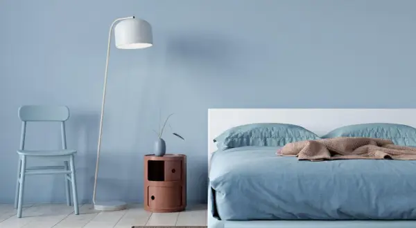 Ein hellblaues Schlafzimmer mit einem Bett, einem Stuhl und einem Nachttisch. Die schlafzimmer farbgestaltung wirkt beruhigend und modern.
