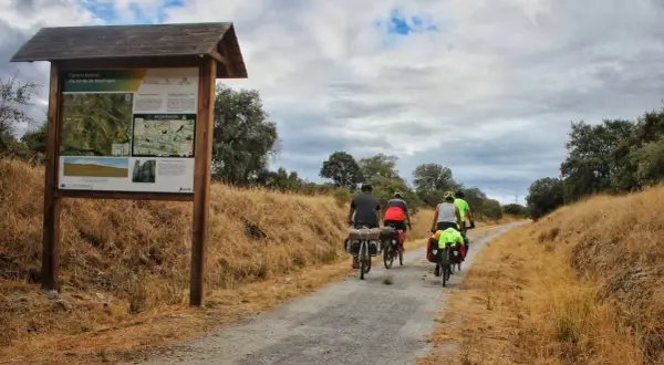 Ciclistas disfrutan de una ruta cicloturista por la Vía Verde de Monfragüe, con un cartel informativo al inicio del camino.