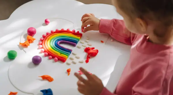 Dziecko tworzy tęczę z plasteliny. Świetne zabawy aktywizujące dla dzieci, rozwijające kreatywność i zdolności manualne.