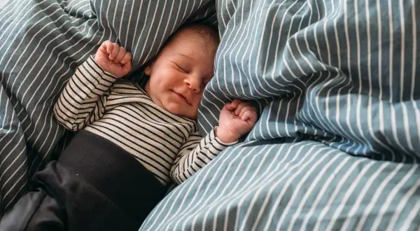 En 5 månaders bebis sover sött i ett randigt täcke. Kanske drömmer hen om att slippa vakna ofta på natten.