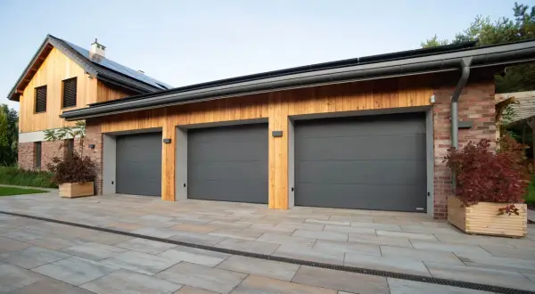 Tre moderna garageportar i mörkgrått framför ett hus med träfasad och tegelfasad.