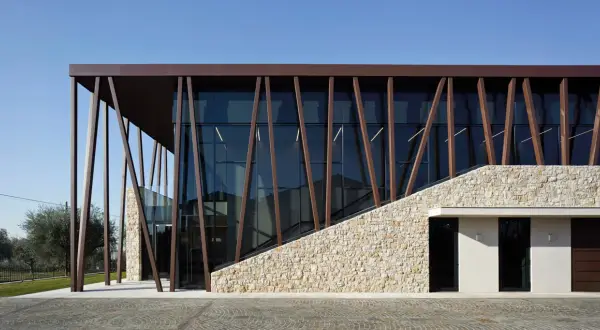 Edificio moderno con facciata in pietra e vetro, travi inclinate in metallo marrone. Un'architettura che evoca i valetti di Bardolino.