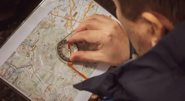 Hombre consultando un mapa profesional y una brújula en un entorno natural.