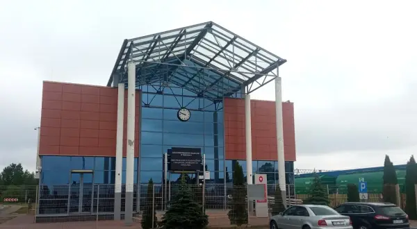 Nowoczesny budynek kolejowy w Terespolu, z charakterystycznym szklanym dachem i brązowymi panelami. W tle widać zielone wagony towarowe, a przed budynkiem zaparkowane samochody. To ważny punkt na trasie Terespol-Brześć.