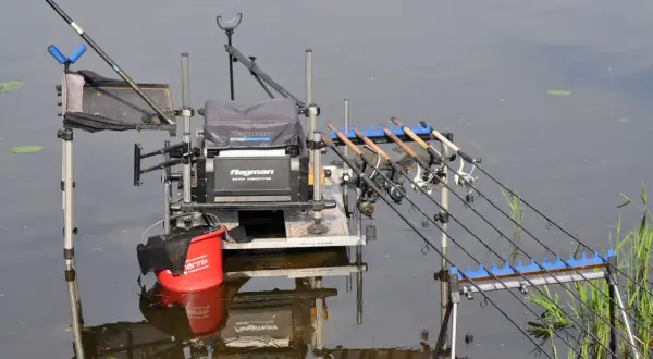 Gotowe stanowisko method feeder z kilkoma wędkami i czerwonym wiadrem, gotowe do łowienia ryb.