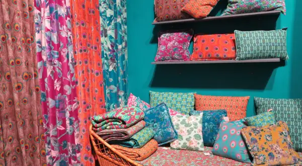 Rideau **couleur corail** et coussins aux motifs floraux et paons, sur un banc en rotin.