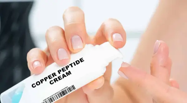 Hände mit gepflegten Nägeln halten eine Tube "Copper Peptide Cream". Die Creme wird auf einen Finger aufgetragen, um ihre positive Wirkung auf die Haut zu zeigen.