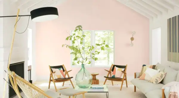 Salotto luminoso con pareti color aragosta tenue, mobili in legno chiaro, un divano beige e sedie con cuscini colorati.