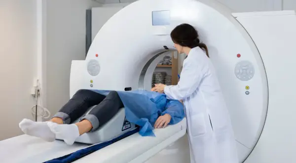Pacjent na stole do tomografii komputerowej, pielęgniarka przygotowuje badanie. Czas oczekiwania na wynik TK na SORze bywa długi.
