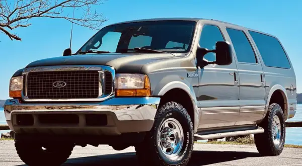Brązowy Ford Excursion z chromowanymi dodatkami i terenowymi oponami stoi na tle błękitnego nieba i nagich drzew.