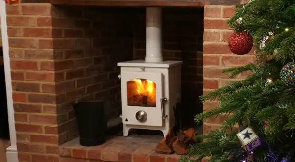 Poêle à pellets blanc dans une cheminée en briques, avec une cheminée décorée pour Noël. Le raccordement poêle à pellet sur cheminée est visible.
