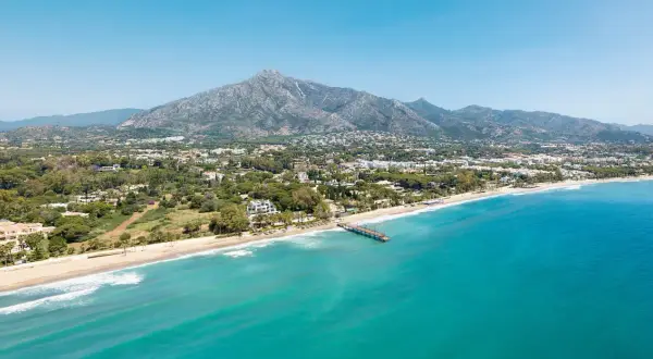 Widok na marbella beach z turkusową wodą, piaszczystą plażą i górami w tle.