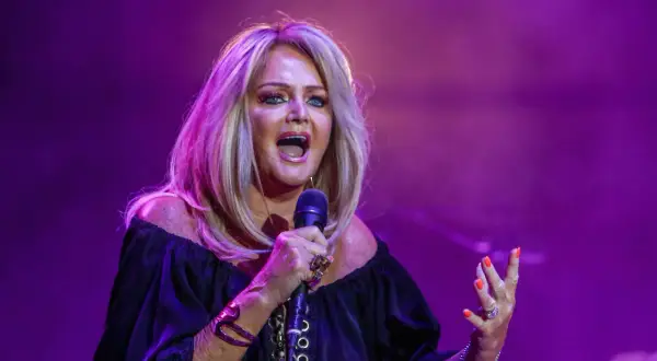 Eine Frau mit blonden Haaren singt leidenschaftlich ins Mikrofon, als würde sie ihre liebsten Karaoke-Songs performen.