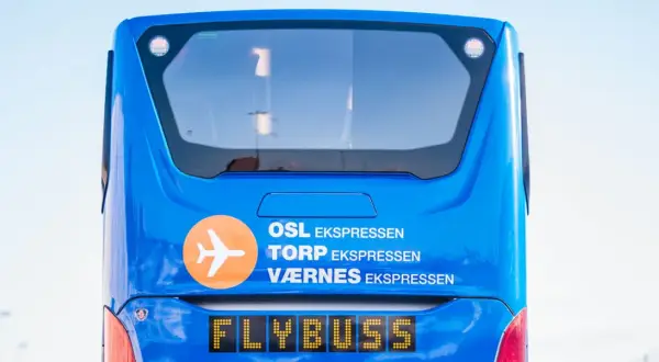 Niebieski Flybuss z napisem "OSL EKS<bos>. TORP EKS PRESEN", gotowy do podróży z lotniska Torp do centrum Oslo.