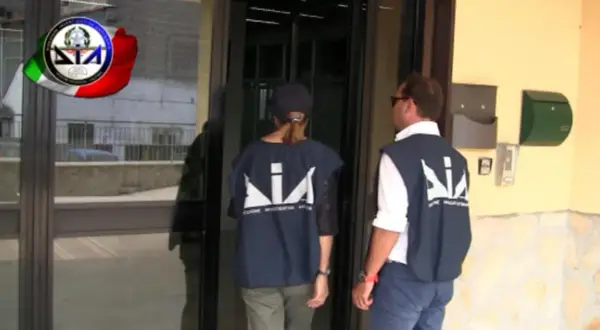 Agenti della DIA, Direzione Investigativa Antimafia, si avvicinano a un ingresso.
