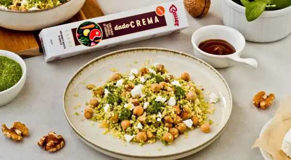 Piatto di cous cous con ceci, formaggio e pesto. Un'idea gustosa per un pasto veloce e saporito.