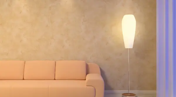 Sofá naranja junto a una lámpara de pie, con una pared de estucado en tonos tierra y cortinas azules al fondo.