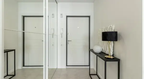 Nowoczesny wiatrołap inspiracje: białe drzwi, lustrzana szafa i elegancka konsola z lampą.