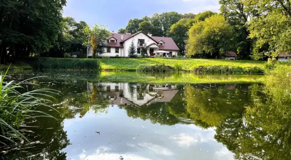 Malowniczy dom seniora w pałacu Jastrzębia Góra, odbijający się w spokojnej tafli stawu, otoczony zielenią.