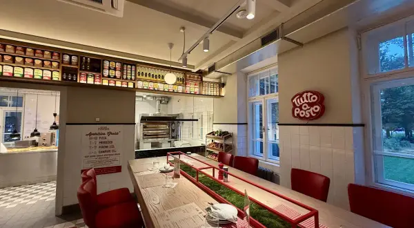 Wnętrze restauracji z czerwonymi krzesłami i długim stołem. Na ścianie wisi neon "Tutto Posto", a nad ladą półki z produktami. Otto Pompieri opinie: warto odwiedzić!