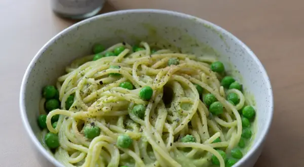 Eine Schüssel mit gesunden Nudeln, garniert mit Erbsen und Kräutern, serviert in einer cremigen grünen Sauce.