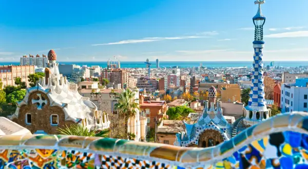 Widok na kolorowe budowle Parku Güell i panoramę miasta, gdzie leży Barcelona, z morzem w tle.