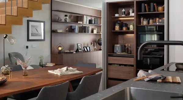 Comedor y zona desayuno cocina con mesa de madera, sillas grises y estanterías empotradas.