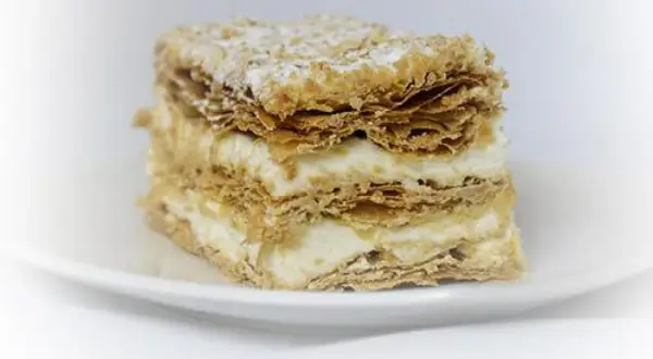 Deliciosa porción de costrada de Soria, con capas crujientes de hojaldre y crema suave, espolvoreada con azúcar glas.