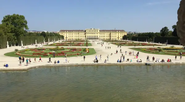 Piękny pałac Schönbrunn i jego ogrody, symbol wiedeńskiej historii. Ludzie spacerują pośród kwiatów i przy stawie.