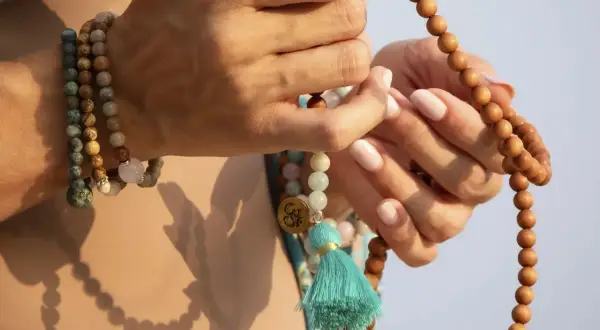 Manos sostienen un japa mala de 108 cuentas de madera. El japa mala 108 cuentas significado se asocia con la meditación y la conexión espiritual.