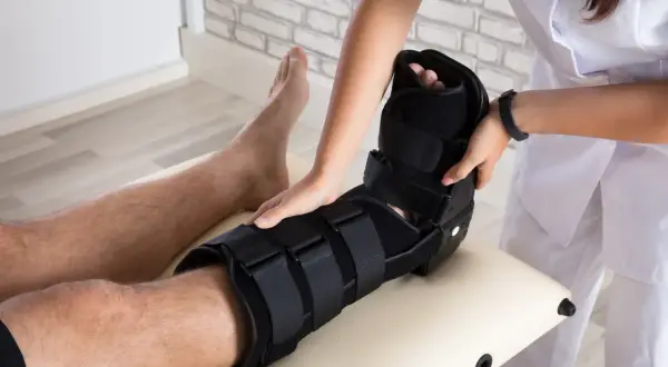 Fizjoterapeuta zakłada pacjentowi stabilizator na nogę, pokazując różne rodzaje gipsu medycznego.