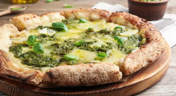 Pizza rustique au pesto, garnie de fines tranches de pommes de terre et de fromage fondant, décorée de feuilles de basilic frais.