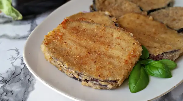 Fette dorate di cordon bleu di melanzane, impanate e fritte, servite su un piatto bianco con foglie di basilico fresco.