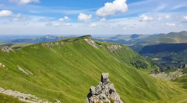 Zielone, faliste wzgórza Masywu Centralnego we Francji pod błękitnym niebem z chmurami.