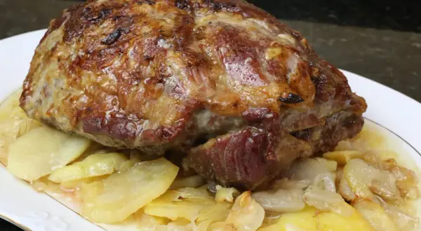 Cabezada de cerdo asada, jugosa y dorada, servida sobre patatas y cebolla caramelizada en un plato blanco.