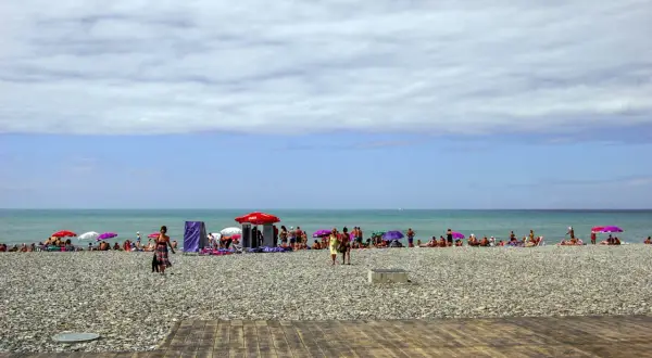 Tłum ludzi wypoczywa na kamienistej plaży w Batumi. Kolorowe parasole chronią przed słońcem.