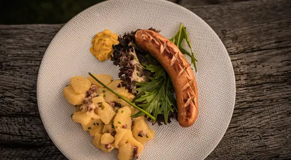 Herzhafter salat zur bratwurst mit Kartoffelsalat, Senf und frischem Grün auf einem Teller.